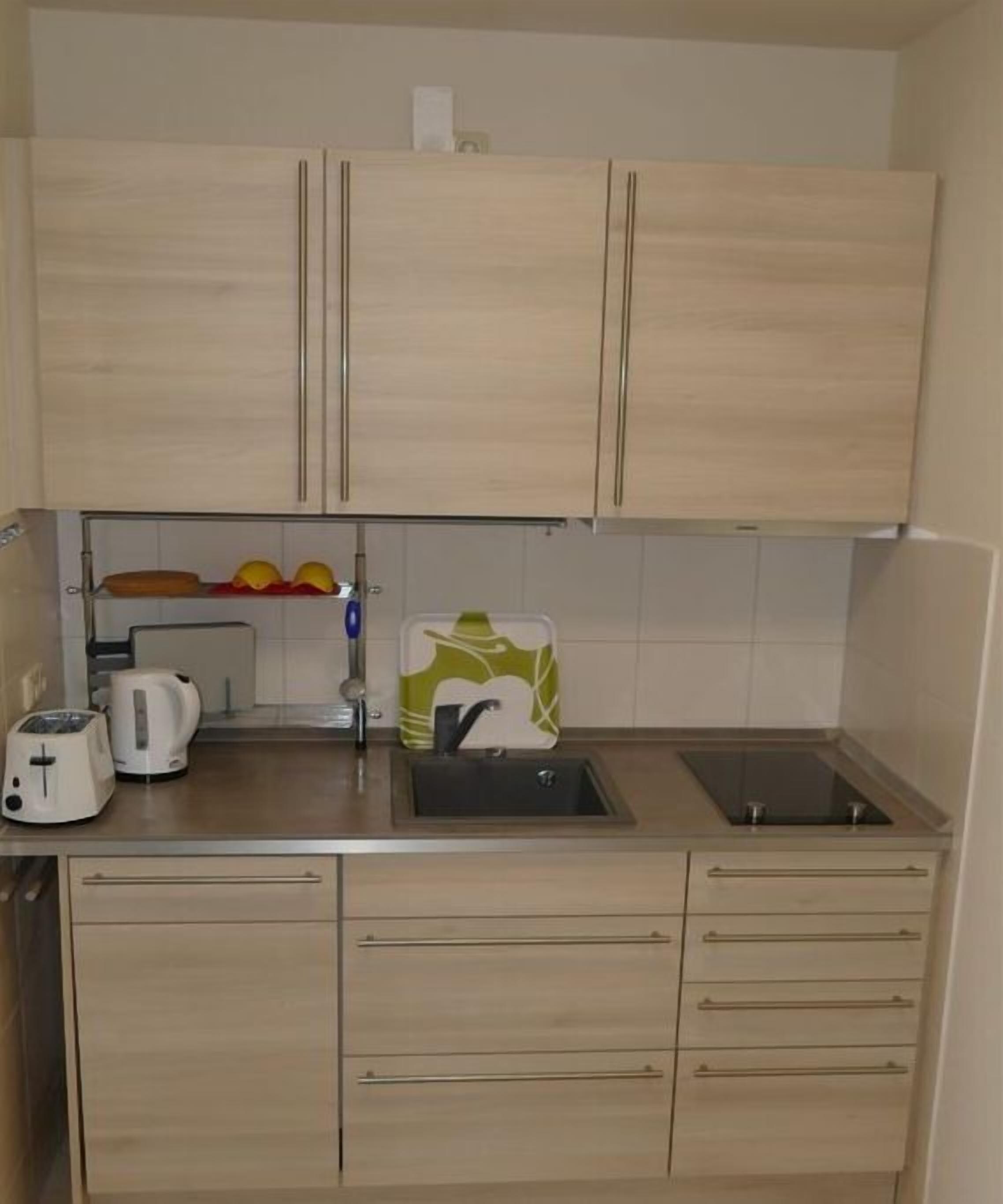 A compact kitchen with two cabinets, a sink, a toaster, and a kettle.