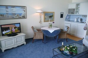 A living room with a television, a dining table with chairs, a kitchen area, and a blue carpet. - Villa Fortuna by the sea, 1st floor (Seebad Bansin)