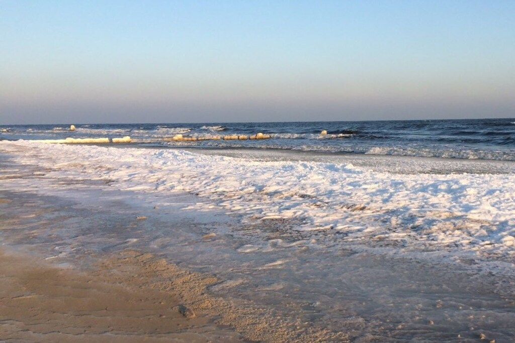 A beach with a frozen shoreline and waves in the background.