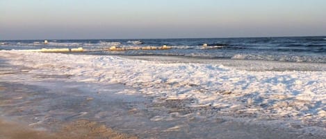 A beach with a frozen shoreline and waves in the background.