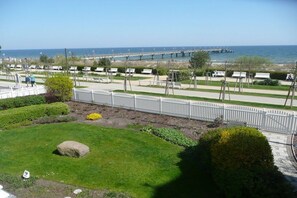 Un parc côtier avec une clôture blanche, des zones herbeuses et une jetée visible au loin.