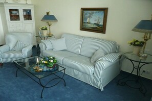 A room with a striped sofa, a glass coffee table with flowers, a cabinet with glass doors, and two lamps. - Villa Fortuna by the sea, 1st floor (Seebad Bansin)