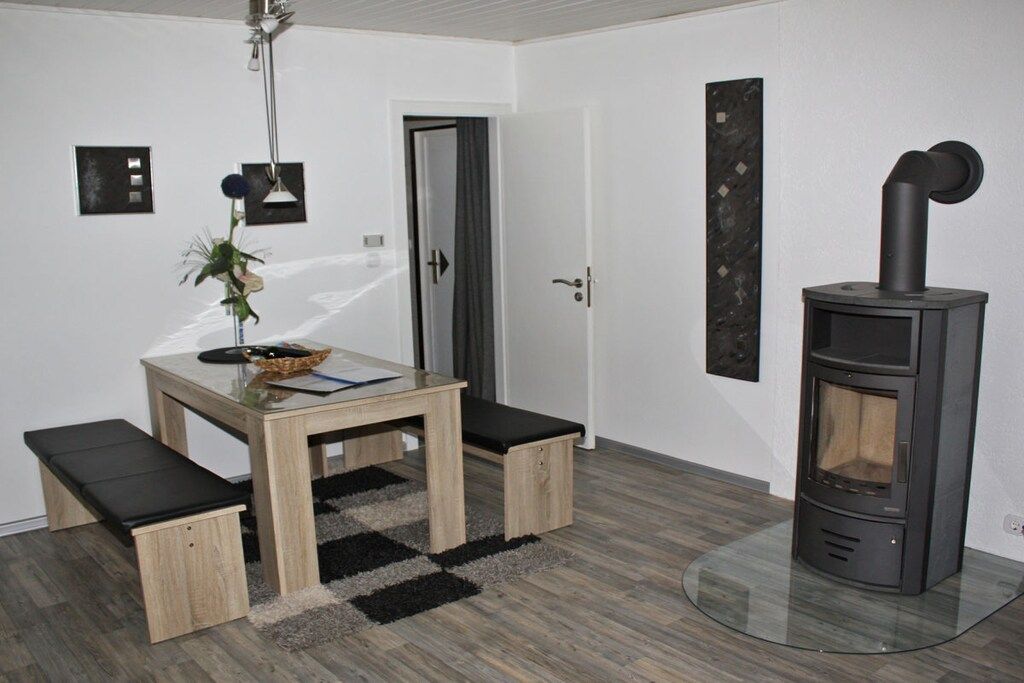 A room with a wooden table, benches, a glass stove, and a door.