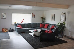 Ein modernes Wohnzimmer mit einem grauen Ecksofa, einem schwarzen Sessel, einem Couchtisch und einer Topfpflanze.