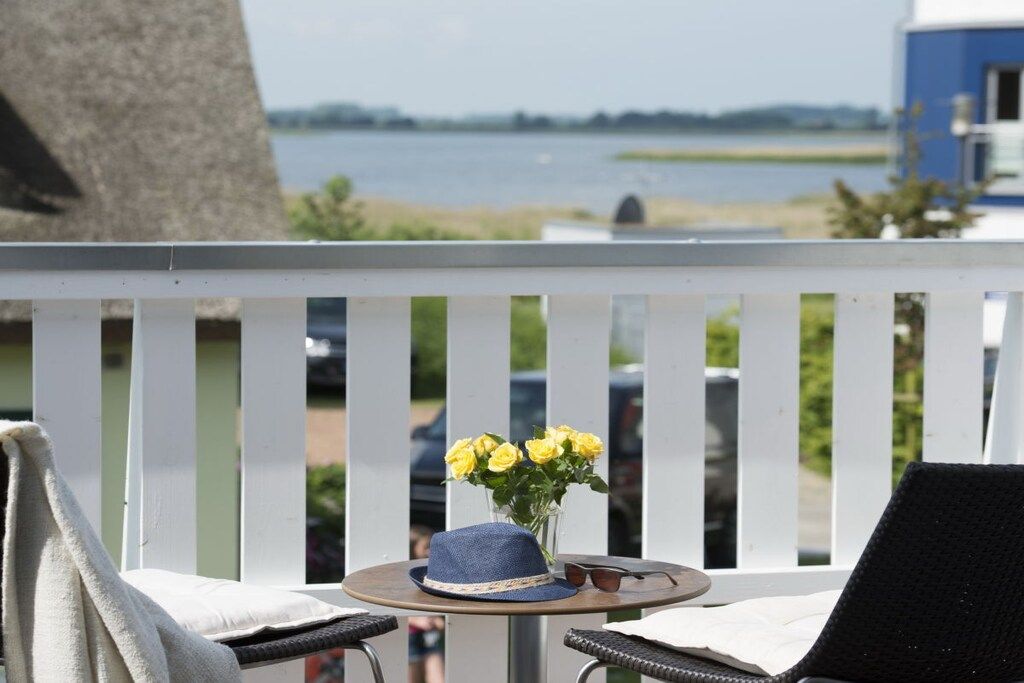A balcony with a view of a body of water, a table with a hat and sunglasses, and a chair.
