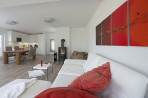A modern living room with a white sofa, a red cushion, and a painting on the wall. - Holiday home in Breege with sauna and Wi-Fi (Breege)