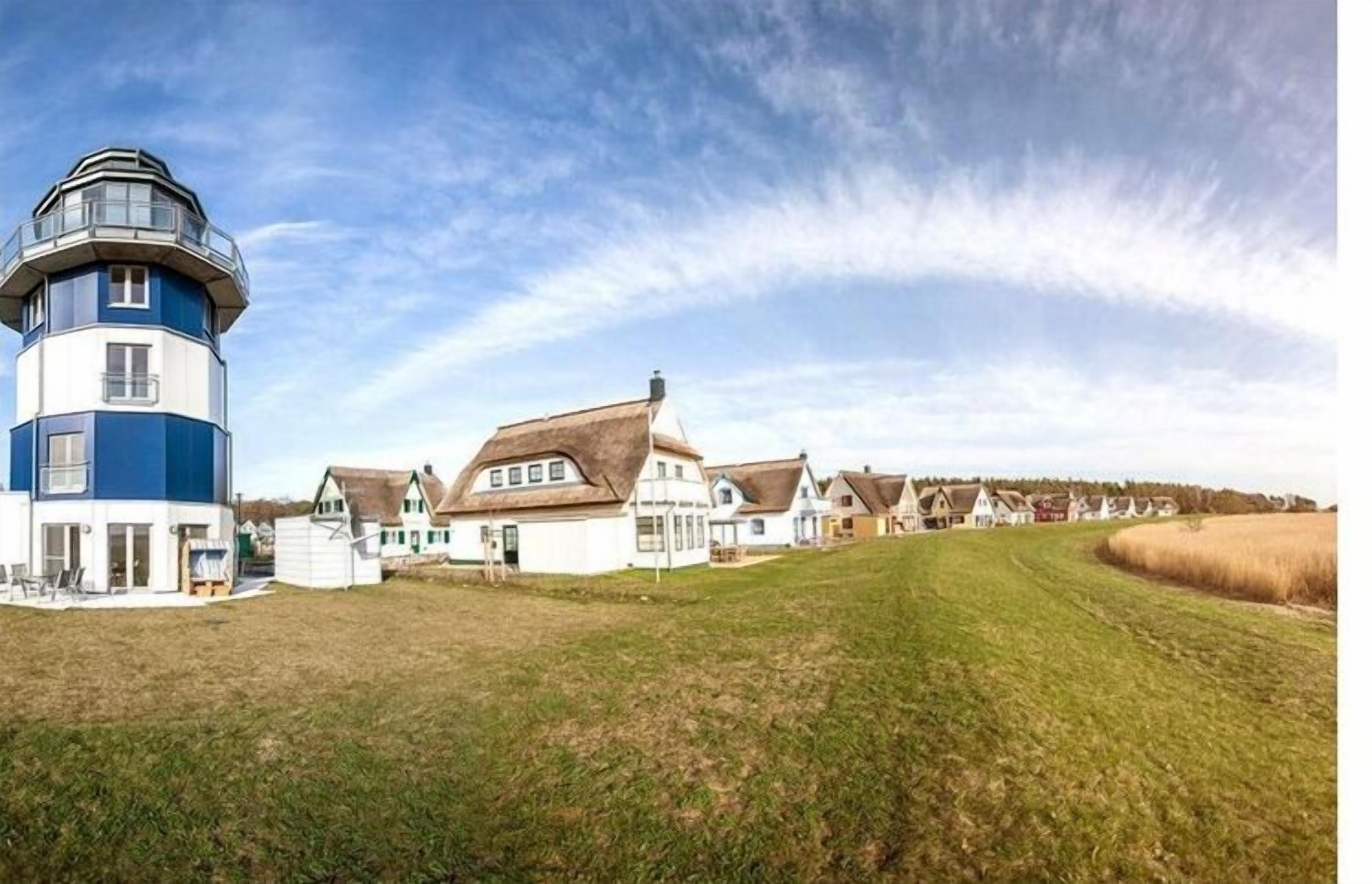 Een kustgebied met woonhuizen, een vuurtoren, huizen met rieten daken en een grasveld.