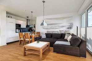 Ein modernes Wohnzimmer mit einem dunkelbraunen Sofa, einem Holztisch und einer Essecke mit weißem Tisch und Stühlen.