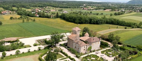A castle with a tower, surrounded by manicured gardens and fields.