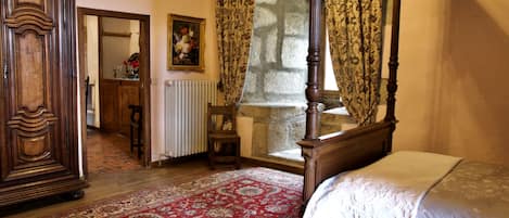 Une chambre à coucher avec un lit à baldaquin, une armoire en bois, un tapis rouge à motifs et un tableau accroché au mur.