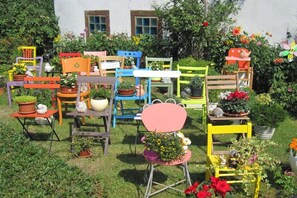 A garden with various colorful chairs and tables, each holding potted plants and flowers. - Holiday apartment with 2 bedrooms (Waltersdorf)