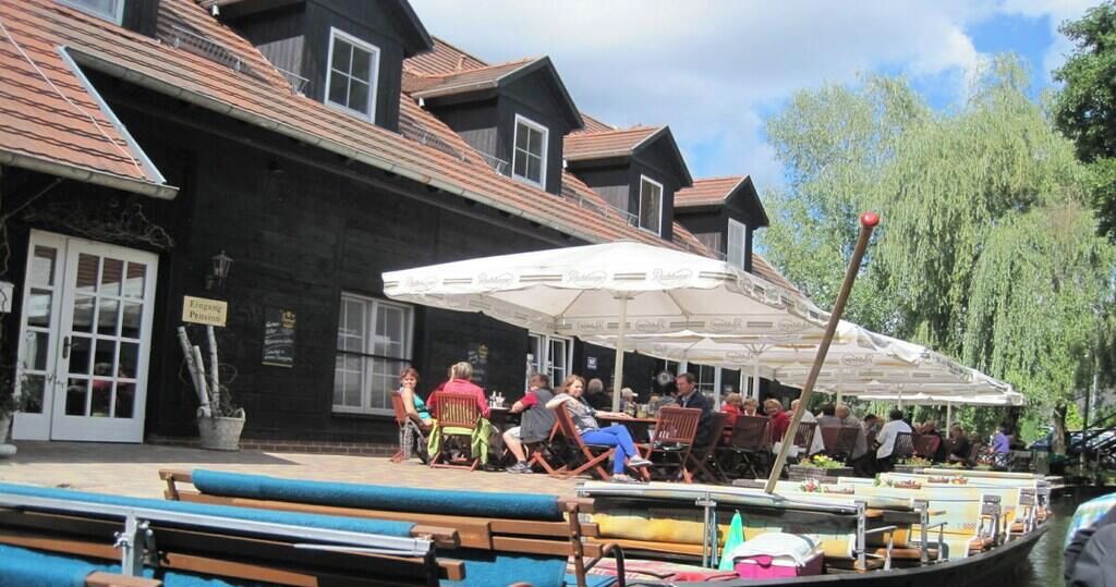 Un restaurant situé au bord de la rivière, avec une terrasse, un bateau amarré à proximité et un bâtiment à la façade sombre.