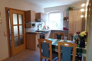 A compact kitchen with a microwave, stove, and wooden cabinets. There is a dining area with a table and chairs. - Holiday apartment with 2 bedrooms (Waltersdorf)