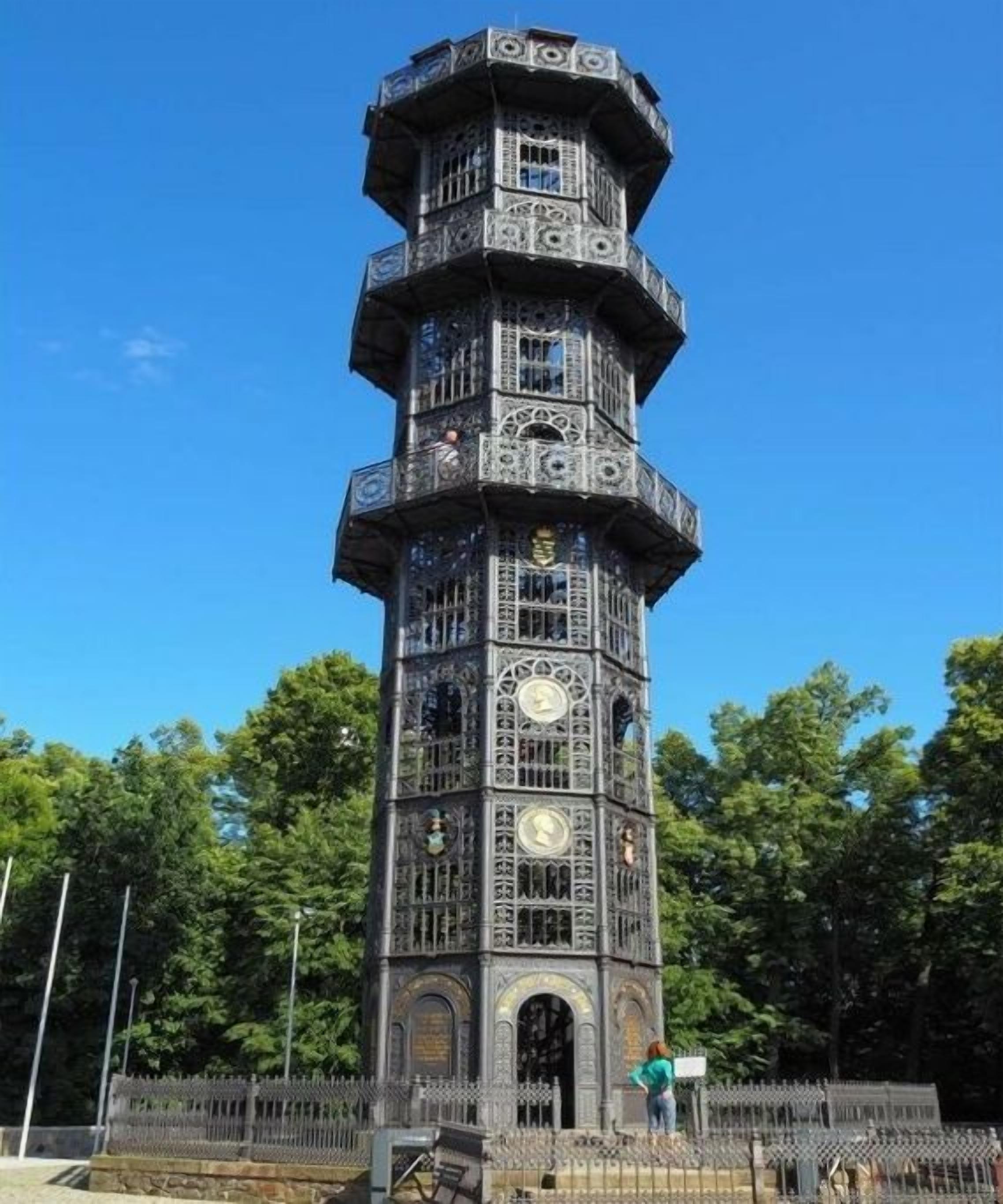 A multi-tiered tower with intricate metalwork and clocks, surrounded by a fence.