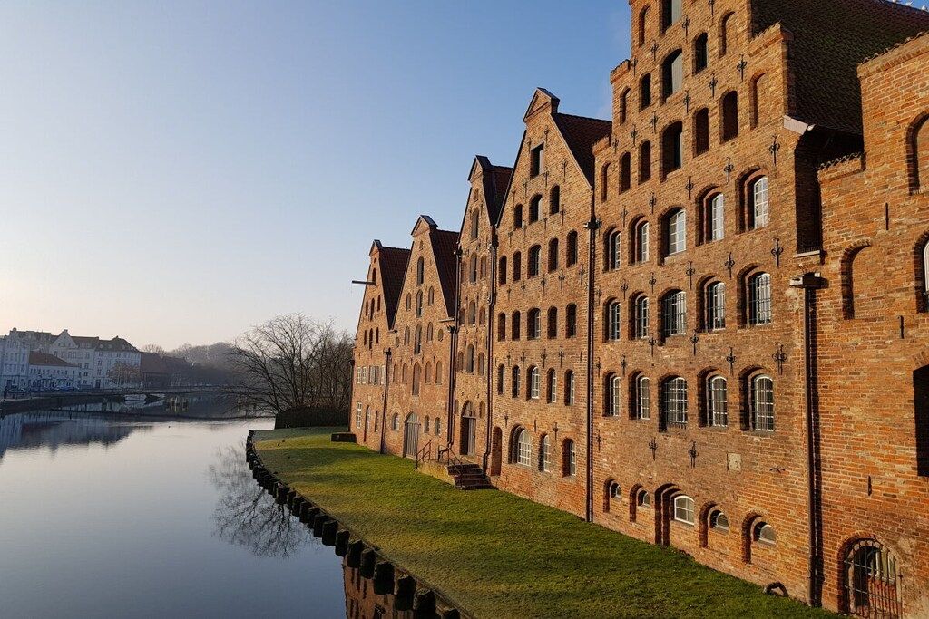 A large brick building with multiple windows and a reflection in the water.