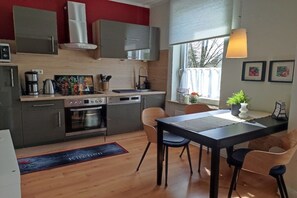 A compact kitchen with modern appliances, a dining area with a table and chairs, and a window with a view of the outside. - Holiday apartment in Lübeck with barbecue (Lübeck)