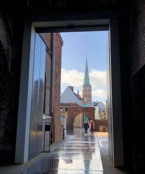 Un pasillo interior con vista a un edificio con techo verde y un arco de ladrillo.