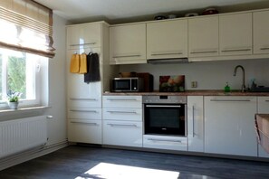 Eine Küche mit weißen Schränken, einer Mikrowelle, einem Backofen und einem Fenster mit Jalousien.