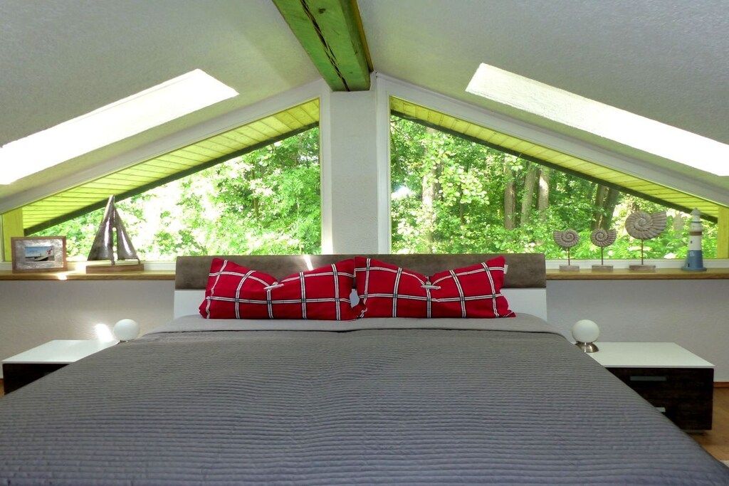Quarto com cama grande, claraboias e vista para árvores.