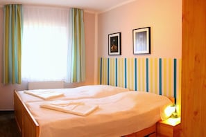 Ein Hotelzimmer mit einem Bett, einem Nachttisch, einem Fenster mit Vorhängen und zwei gerahmten Bildern an der Wand.