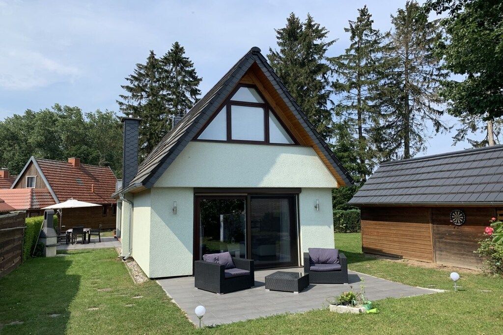 Uma casa moderna com telhado inclinado, uma grande porta de correr de vidro e área de estar externa.