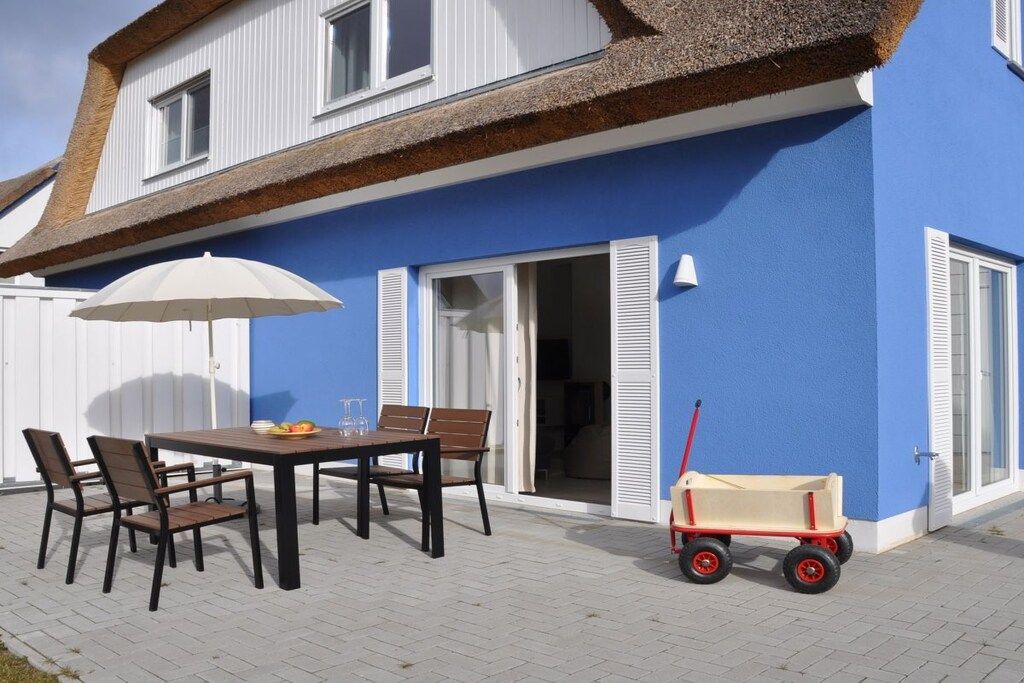 Eine Terrasse mit Tisch und Stühlen, einem weißen Sonnenschirm und einem roten Spielzeugwagen.