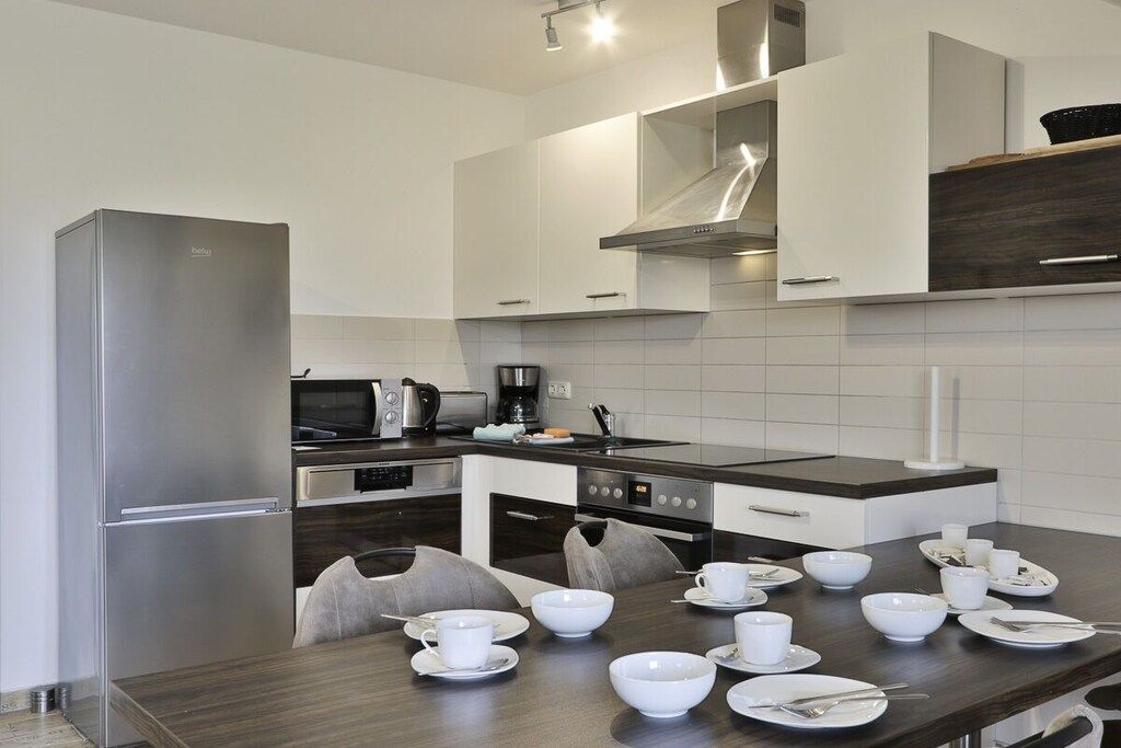 A modern kitchen with stainless steel appliances, white cabinetry, and a dining area with a dark wood table and white chairs.
