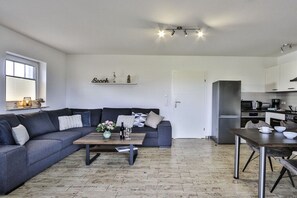 Ein modernes Wohnzimmer mit einem grauen Sofa, einem Holztisch und einer Küchenzeile mit Kühlschrank und Mikrowelle.