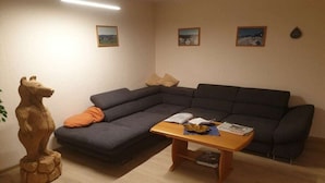 Ein Wohnzimmer mit einem Ecksofa, einem Holztisch und einer Bärenstatue.
