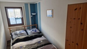 Ein Einzelbett mit Kopfteil, ein Fenster mit Vorhängen, eine Stehlampe und ein Holzschrank.