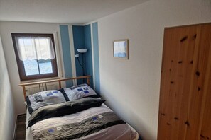 Una cama individual con cabecera, una ventana con cortinas, una lámpara de pie y un armario de madera.