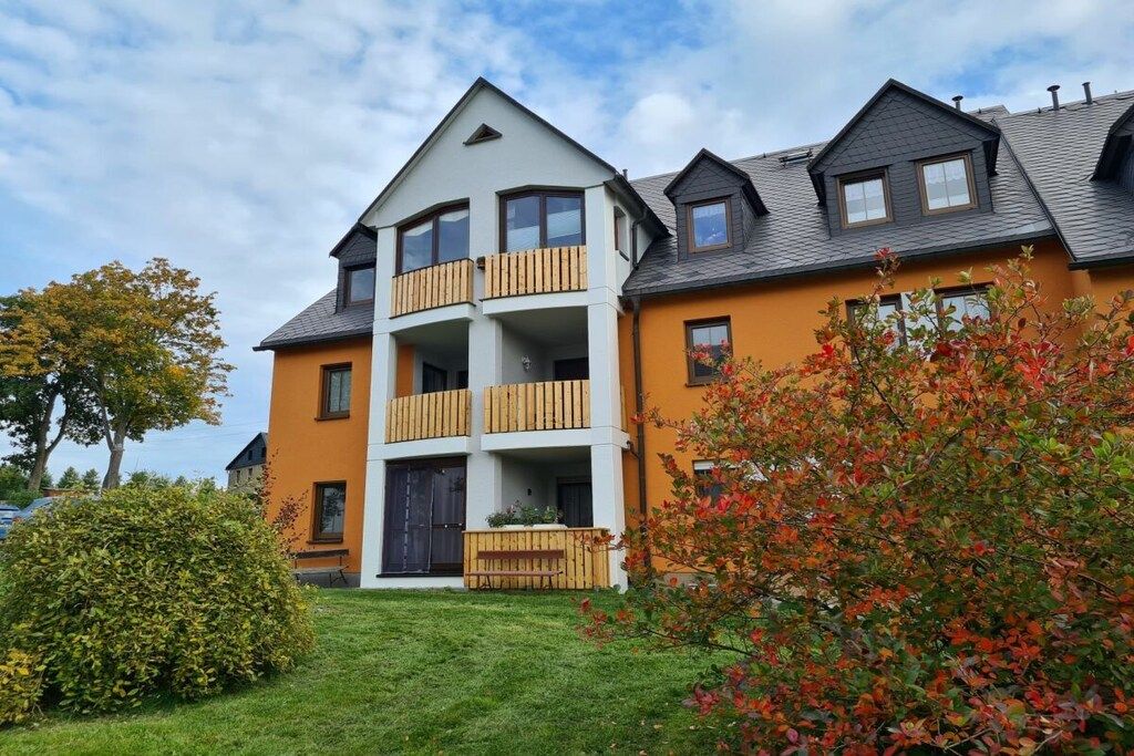 A multi-story residential building with balconies, a well-maintained lawn, and mature trees.