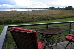 A balcony with two chairs and a table, overlooking a grassy field and a body of water. - Holiday apartment with 2 bedrooms (Breege\/ Juliusruh OT Breege)