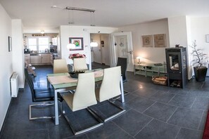 Eine moderne Küche mit dunklen Fliesen, ein Essbereich mit Tisch und Stühlen sowie ein Wohnbereich mit Kamin.