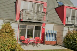 Ein zweistöckiges Haus mit einem Balkon, einer Terrasse mit Gartenmöbeln und einem überdachten Sitzbereich.