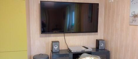 Una habitación con una televisión de pantalla plana montada en la pared, una mesita con un objeto decorativo y un cesto de basura.