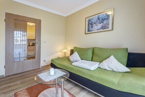 A room with a green sofa, a small glass table with a white candle, a wooden door with a mirror, and a framed picture on the wall. - At Schloonsee, Apartment C-5 (Seebad Heringsdorf)