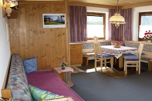 Ein gemütliches Zimmer mit einer Holzwand, einem Sofa, einem Esstisch mit Stühlen und einem Fenster mit Vorhängen.