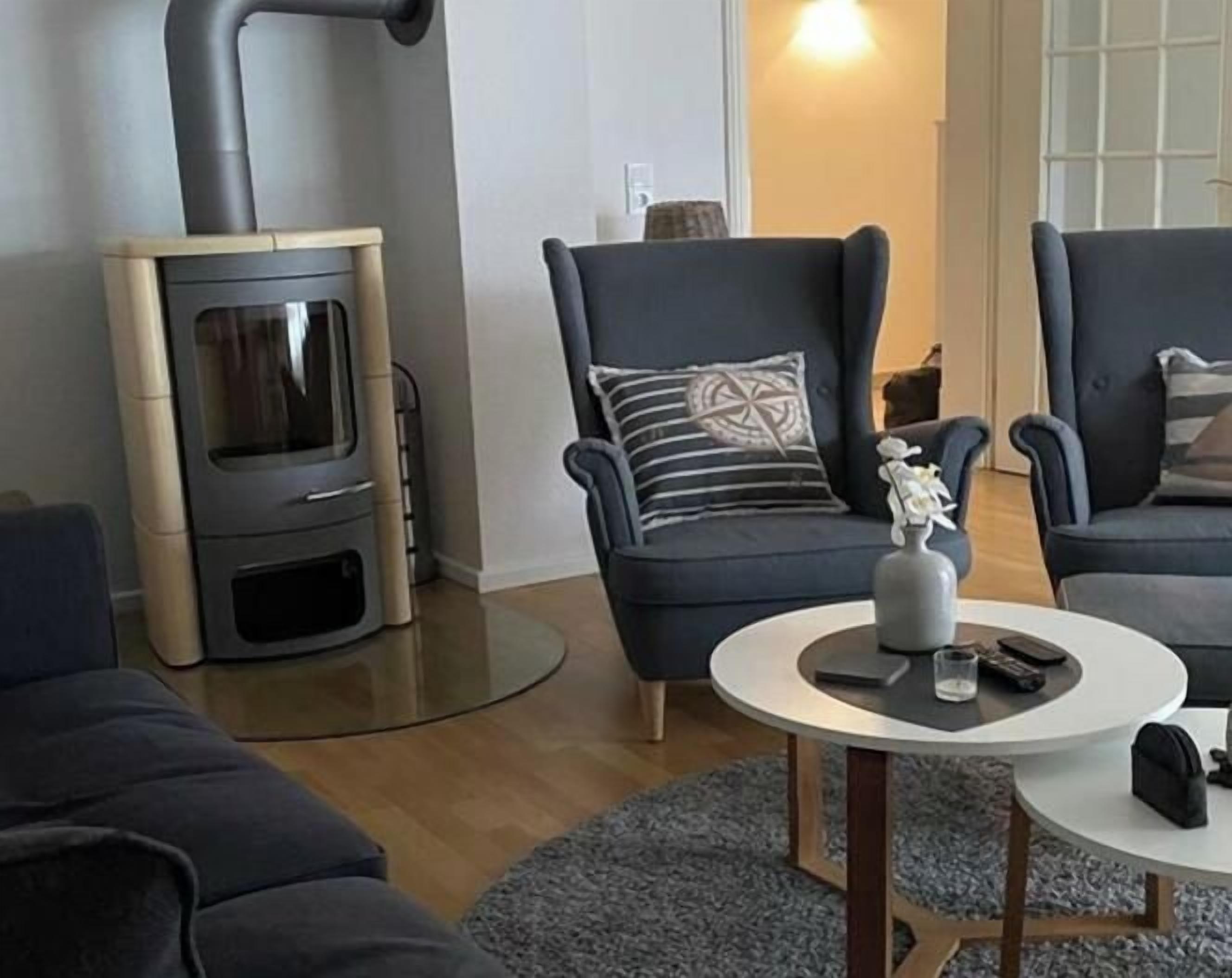 Ein Wohnzimmer mit modernem Kamin, zwei dunklen Sesseln, einem runden Couchtisch und einem Teppich.