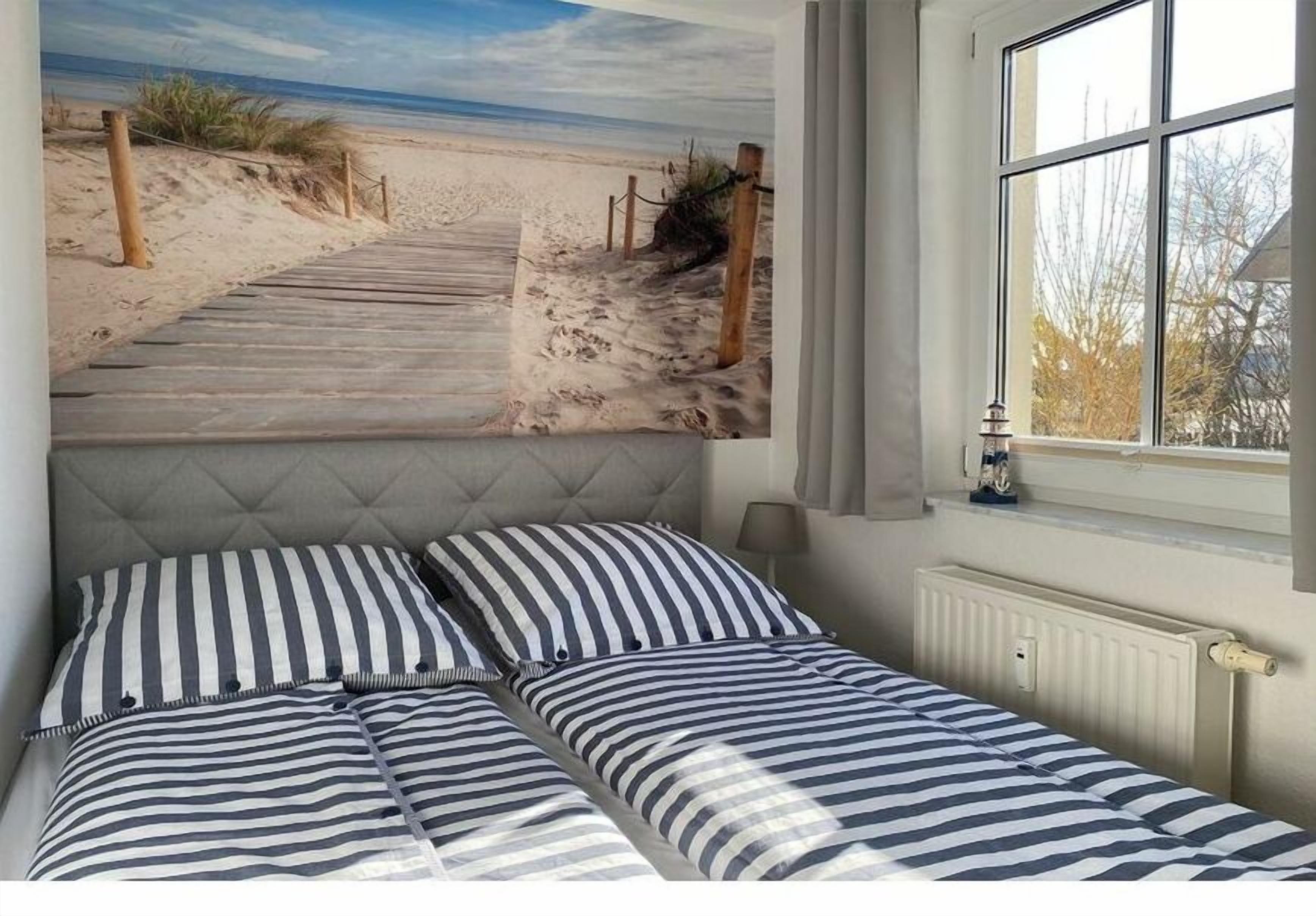 Een slaapkamer met een bed, een raam en een strandschildering op de muur.