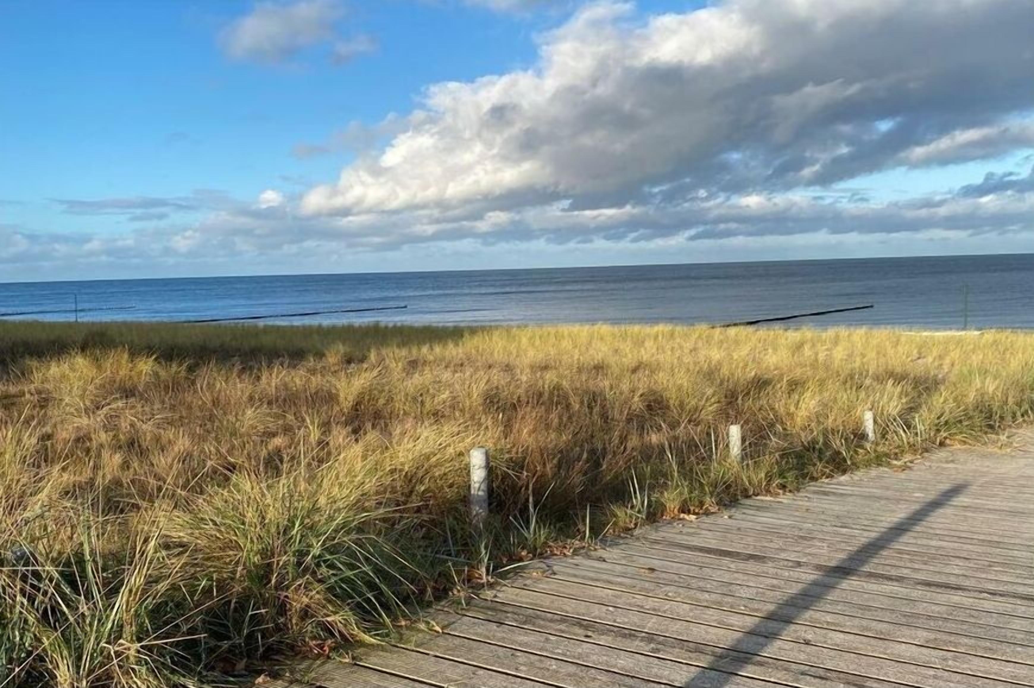 Une promenade en bois qui mène à une plage bordée de dunes herbeuses.
