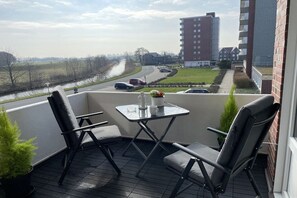 Ein Balkon mit zwei Stühlen und einem Tisch, mit Blick auf eine Straße und Gebäude.
