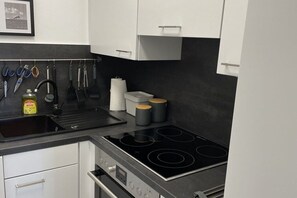 A modern kitchen with a black countertop, stainless steel appliances, and white cabinets. - Apartment No. 8 Horumersiel (26434 Horumersiel)