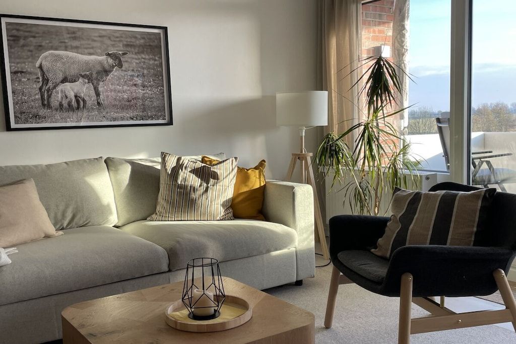 A living room with a sofa, armchair, coffee table, and a framed photograph on the wall.