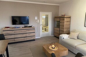 Ein modernes Wohnzimmer mit Flachbildfernseher, Holzmöbeln, einer Couch und einem Couchtisch mit Kerze.