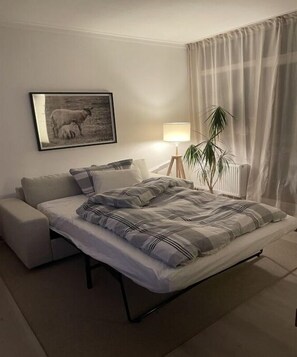 Ein Schlafzimmer mit einem Bett, einem Nachttisch, einer Lampe, einer Pflanze und einem gerahmten Bild an der Wand.