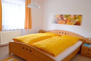 A room with a bed, a bedside table, a lamp, a window with curtains, and a wall painting. - Romantic mountain accommodation on the 1st floor (Leutasch)