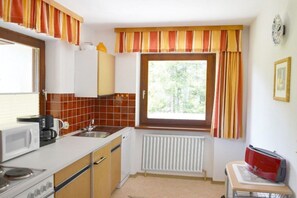 A compact kitchen with a microwave, stove, and sink. There's a window with curtains, a radiator, and a small table with a red appliance. - Romantic mountain accommodation on the 1st floor (Leutasch)