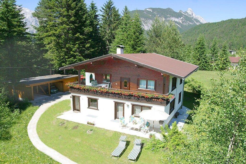 A two-story house with a balcony, a patio with outdoor furniture, and a mountain backdrop.