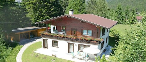 A two-story house with a balcony, a patio with outdoor furniture, and a mountain backdrop.